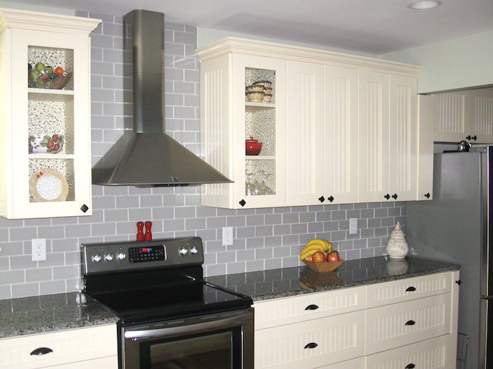 bowl of fruit, on a glossy grey counter top, near a wall, with creamy grey subway tile pattern, white kitchen cabinets