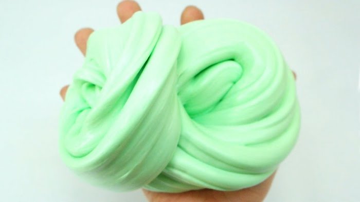 little hand holding a pile of minty green goop, twisted into a knot-like shape, fluffy slime recipe, off-white background