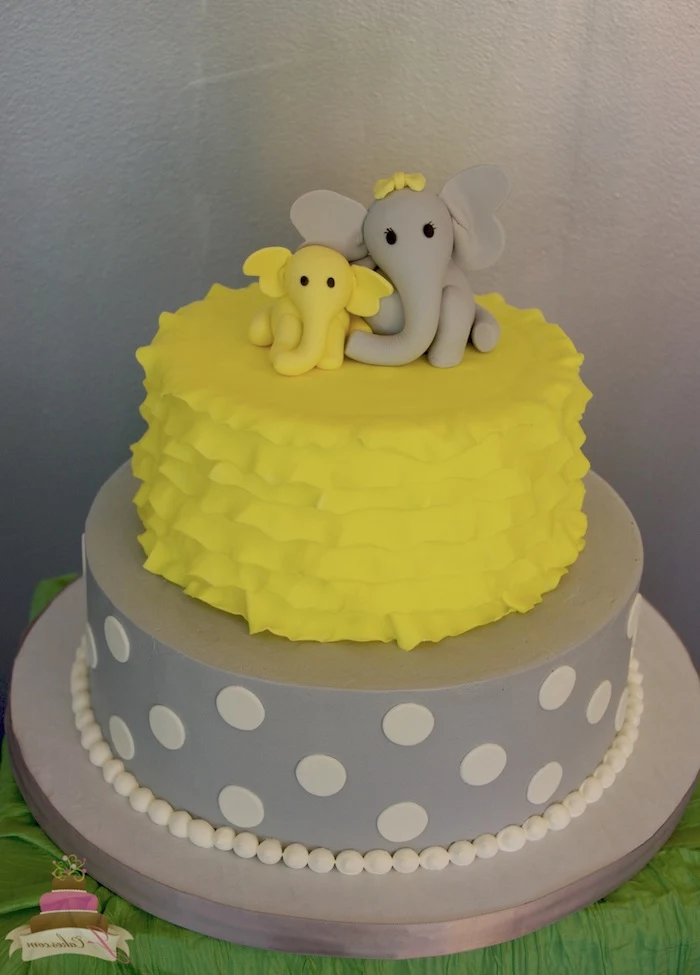 child and mother elephant, made from yellow and grey fondant, topping a grey and yellow elephant baby shower cake, decorated with frills and white polka dots