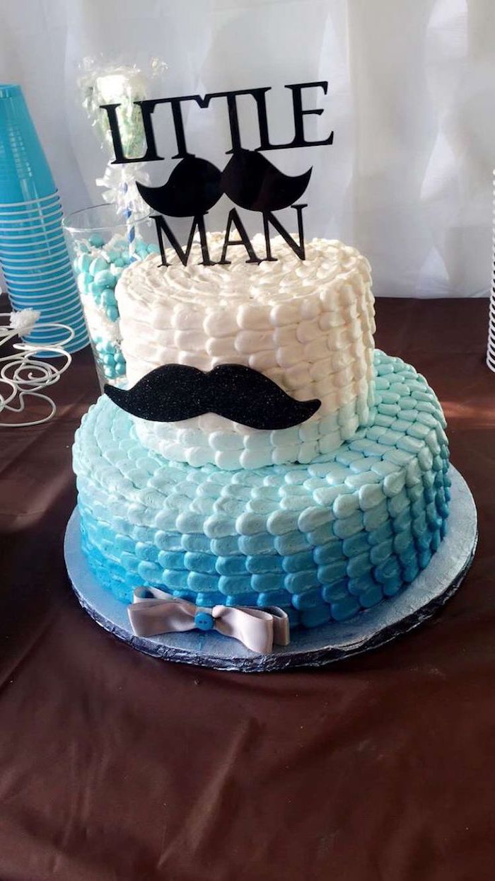 little man written in black, on a cake topper with a mustache, decorating a blue and white, ombre effect cake, with a mustache and a grey ribbon