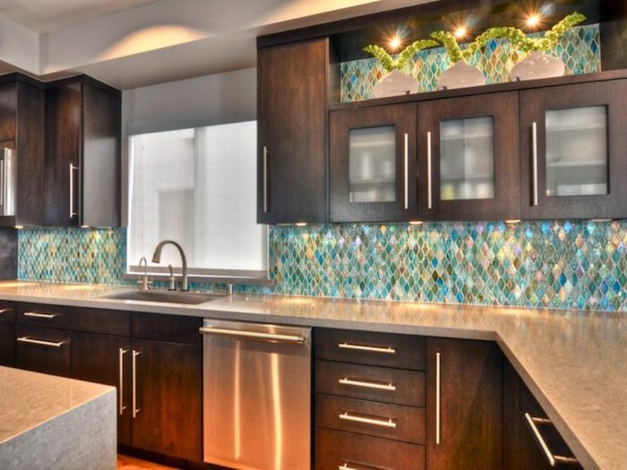 fish scale effect wall, in iridescent turquoise, green and pink, inside a kitchen, with dark brown wooden cabinets, and light grey counter tops