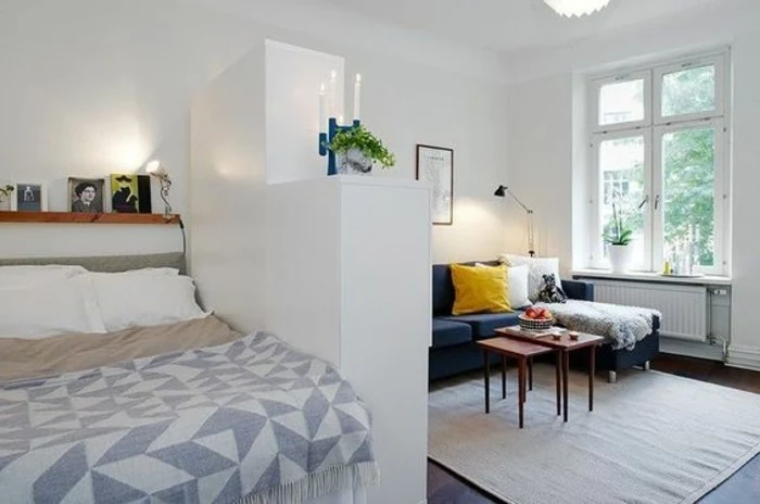 corner sofa in dark blue, with white and yellow cushions, and two small coffee tables, living room furniture for small spaces, sleeping area separated by a white wardrobe
