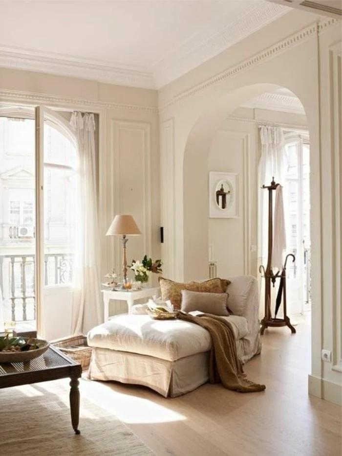 fainting couch in cream, with beige cushions, inside a room with cream walls, an open terrace door, and an archway detail