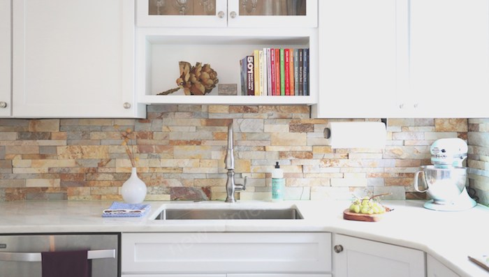 stacked stone backsplash, in beige and grey tones, in a kitchen with white cabinets, and matching white counter tops