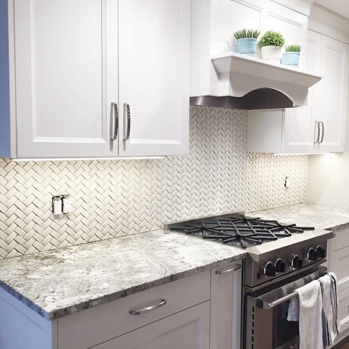 off white kitchen backsplash, with small tiles, in a herringbone pattern, stove and white cabinets, grey and white counter top