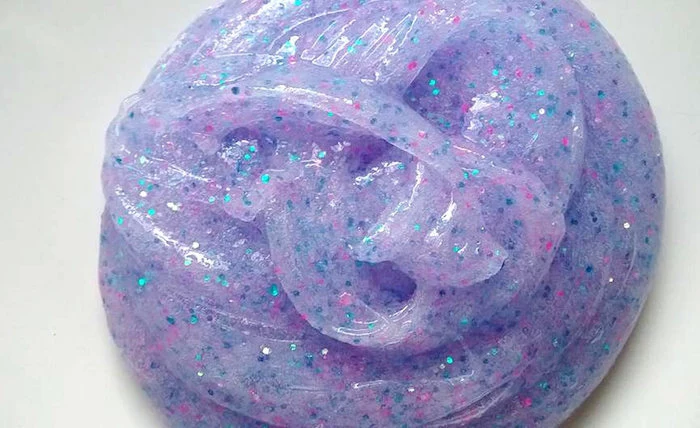 creamy violet elmer's glue slime, twisted and shaped into a roundish form, and decorated with pink, blue and silver glitter