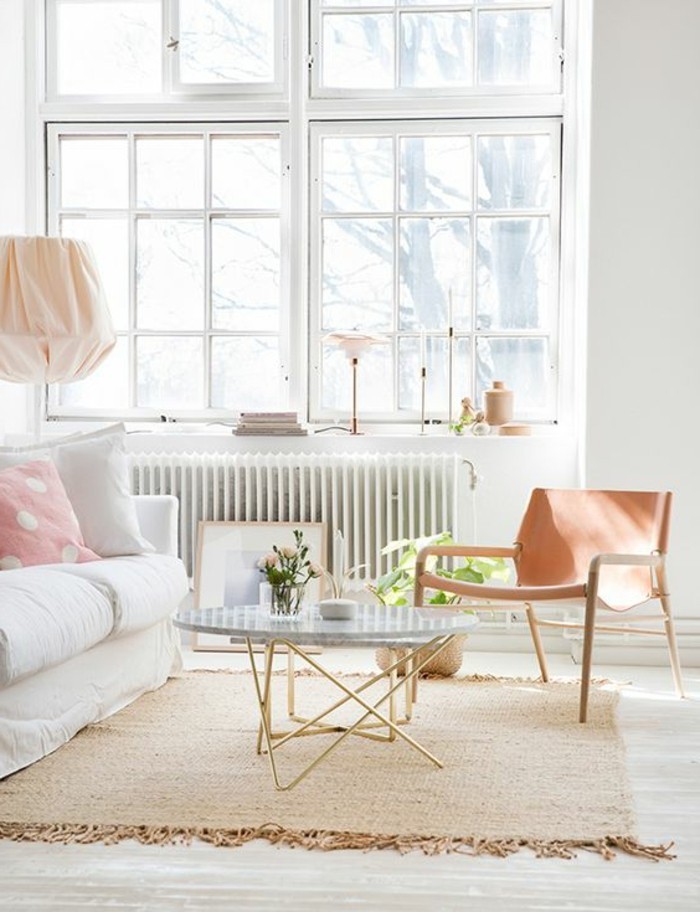 rug in beige with tassels, inside a bright room, with large windows, containing a white sofa, a coffee table, and a peach-colored chair