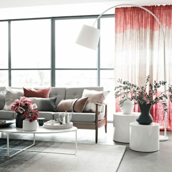 tall lamp in white, near two white stands, with grey and white vases, room setup ideas, pale grey sofa, with several cushions, and a white coffee table, with pink flowers