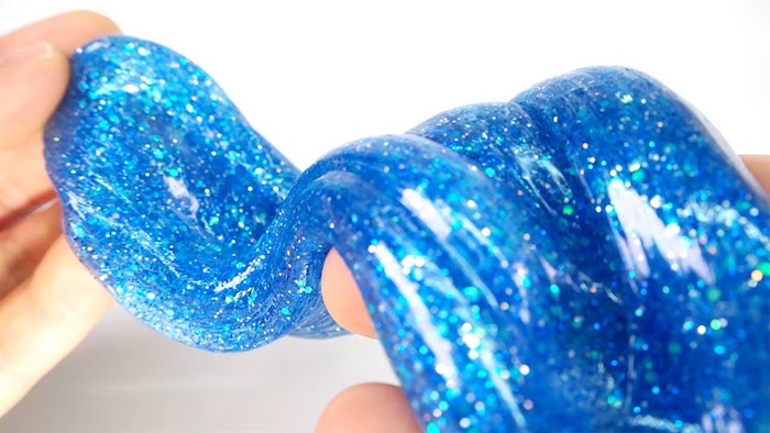 sparkly blue goo, or slime without borax, stretched by two pale hands, gum-like consistency, with pale blue glitter