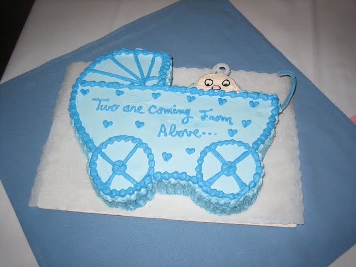 carriage-shaped cake, with a baby peeking from inside, baby shower sheet cakes, decorated with light and dark blue, and cream-colored frosting 