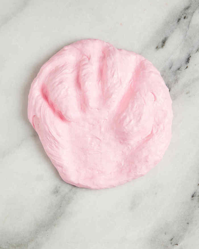 handprint of a child, left in a flattened piece of lumpy and soft, pale pink goo, how to make fluffy slime, marble surface in white, and pale grey