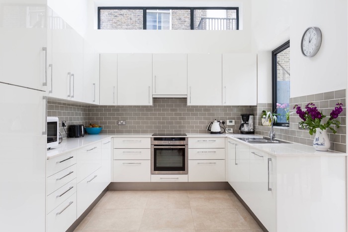 mink brown subway tile kitchen backsplash, in a room with a high ceiling, white kitchen cabinets, and beige tiled floor