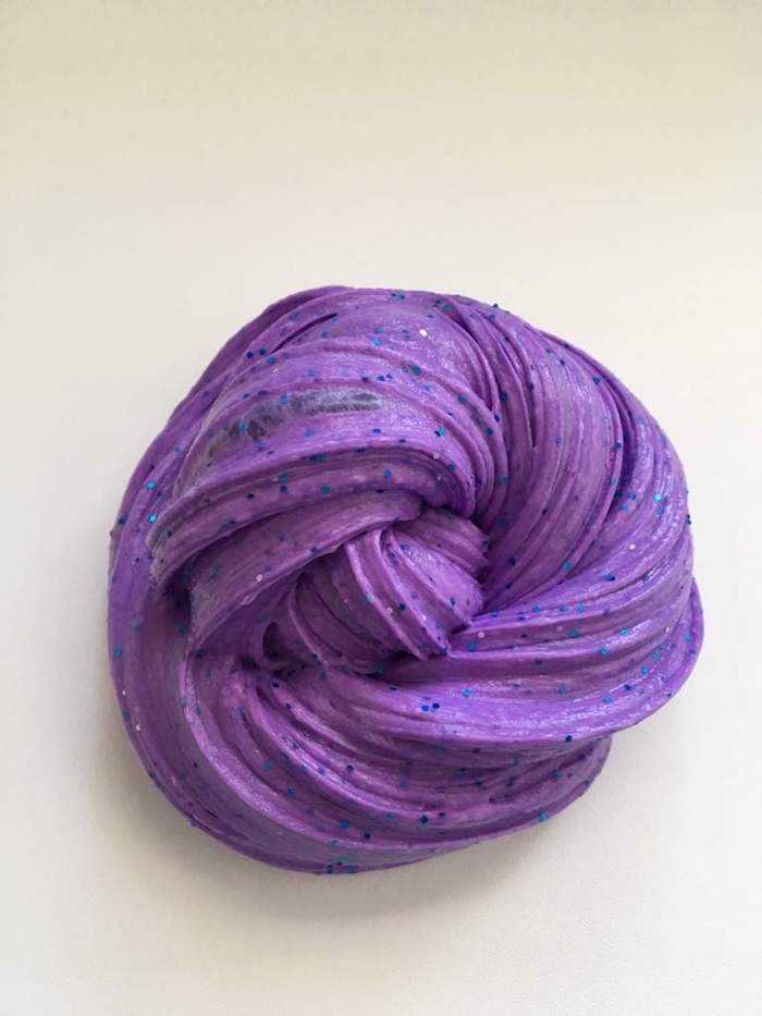fluffy slime in dark purple, decorated with black sparkles, and shaped into a twisted round blob, on a light cream background
