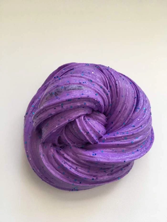 fluffy slime in dark purple, decorated with black sparkles, and shaped into a twisted round blob, on a light cream background
