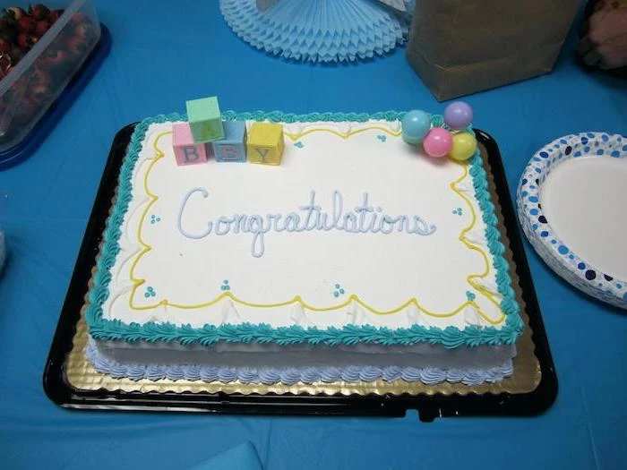 congratulations written in pale blue frosting, on rectangular white sheet cake, with teal and light blue details, and colorful fondant shapes