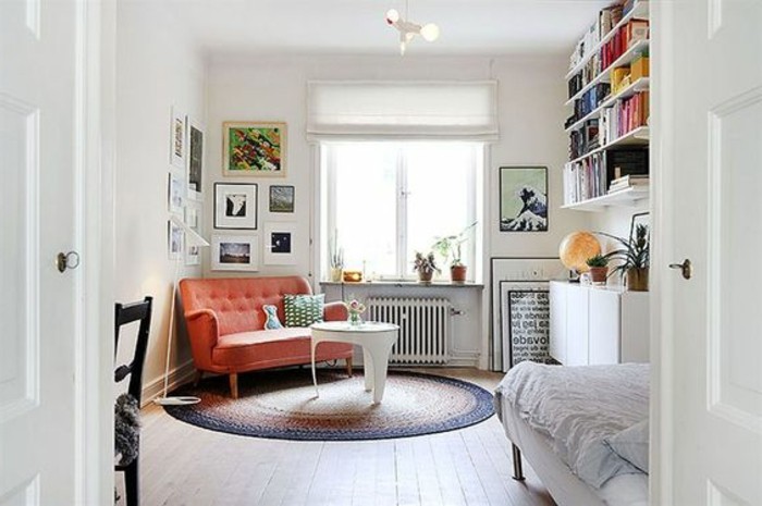 brick red settee, inside a white room, with a round multicolored rug, and a small modern coffee table, living room furniture for small spaces, book shelves and a bed