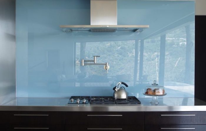 sky blue opaque glass backsplash, smooth and reflective, in a kitchen with black cabinets, a metal counter top, modern faucet and extractor hood