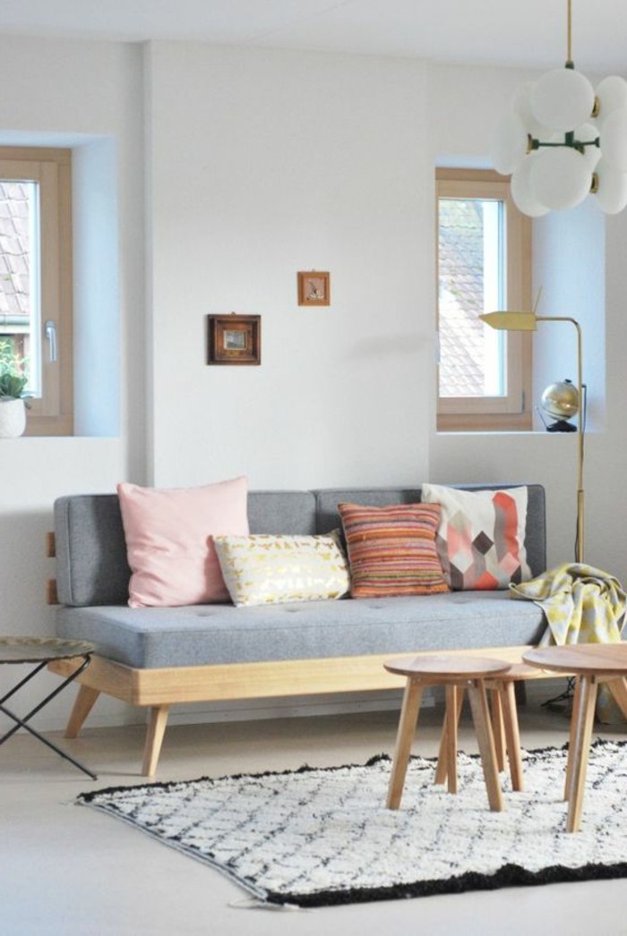 four cushions on a pale grey sofa, inside a room with white walls, and a smooth white floor, couches for small living rooms, black and white fluffy rug, three small wooden coffee tables
