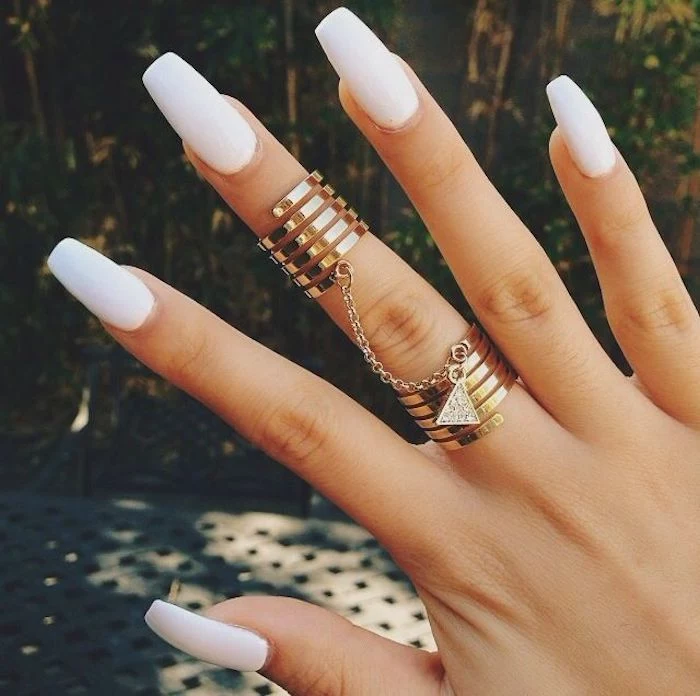 chain linking two golden rings, worn on the middle finger of a hand, with long coffin nails, painted in pure white nail polish