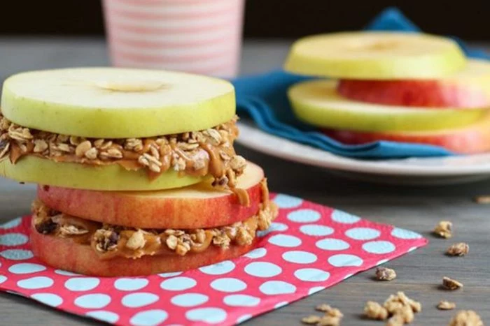 sandwich made from green and red apples, cut into round slices and stacked, with peanut butter and seeds between them