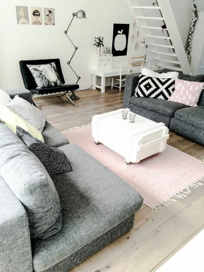 pastel pink rug and cushion, inside a room with grey sofas, simple living room designs, a black chair, white walls and a beige wooden floor