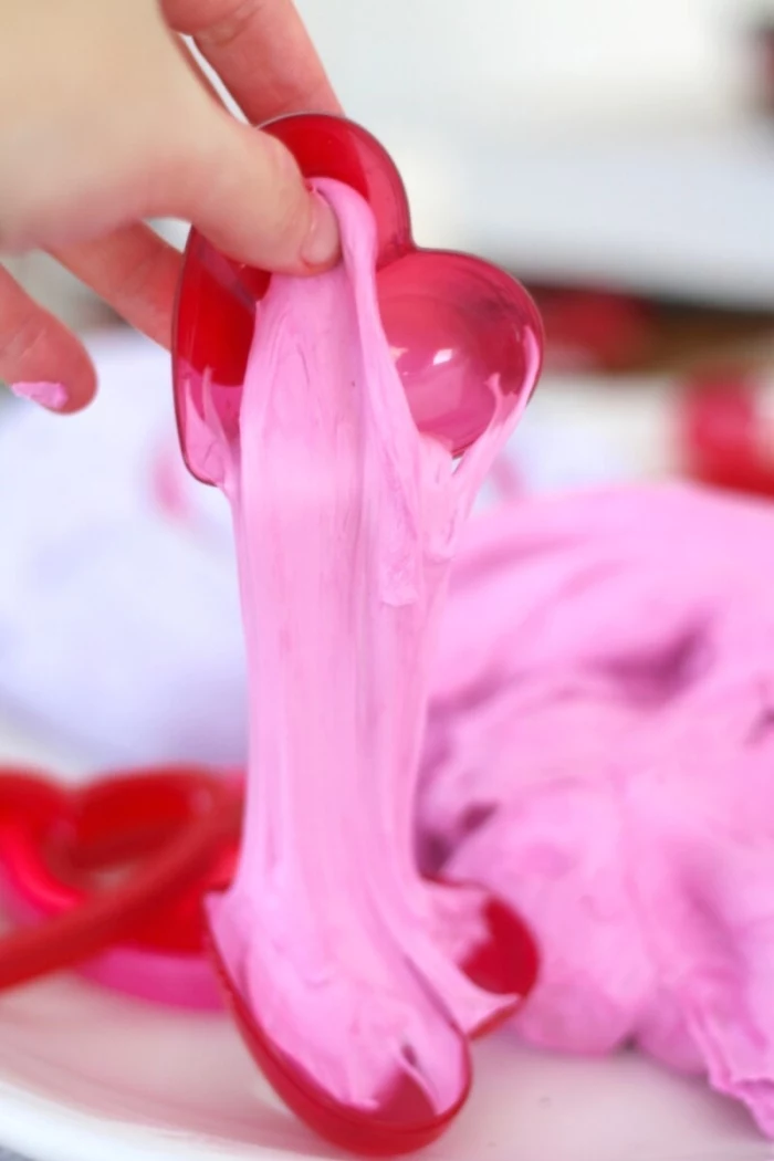 how to make slime with shaving cream, hand holding half of a red plastic container, shaped like a heart, oozing pink fluffy slime