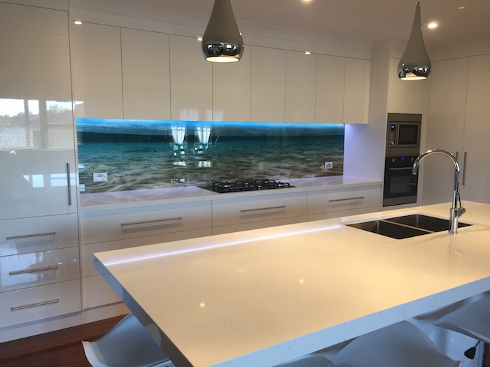 3D effect wall decal, depicting a seashore, creative kitchen back splash, near smooth white cabinets and drawers, and a matching kitchen island