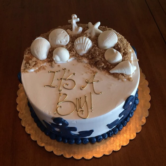beach-inspired cake in white, decorated with dark blue anchors, sand made from brown sugar, and white shell, starfish and anchor shapes, made from fondant