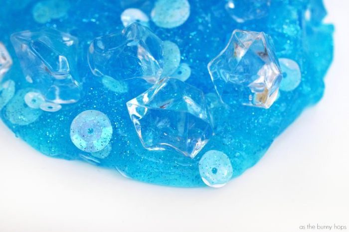 extreme close up of pale turquoise slime, decorated with sequins, and small clear plastic shapes, looking like ice cubes