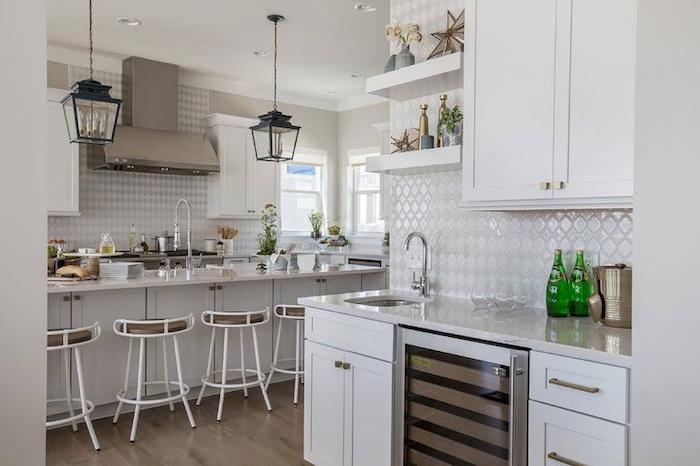 lantern-style lamps hanging from the ceiling, white kitchen cabinets, glossy off-white arabesque backsplash, several stools and a counter top