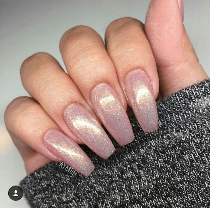 pearly shimmering pink nails, long and oval, with square tips, attached to a hand, holding a grey, salt and pepper knitted sleeve