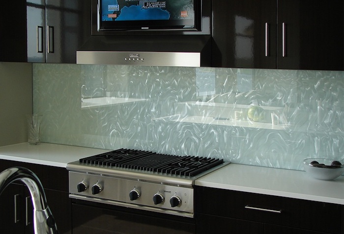 water-effect glass backsplash, in pale blue, with glittering silver details, near glossy and smooth, black kitchen cabinets, and a white counter top