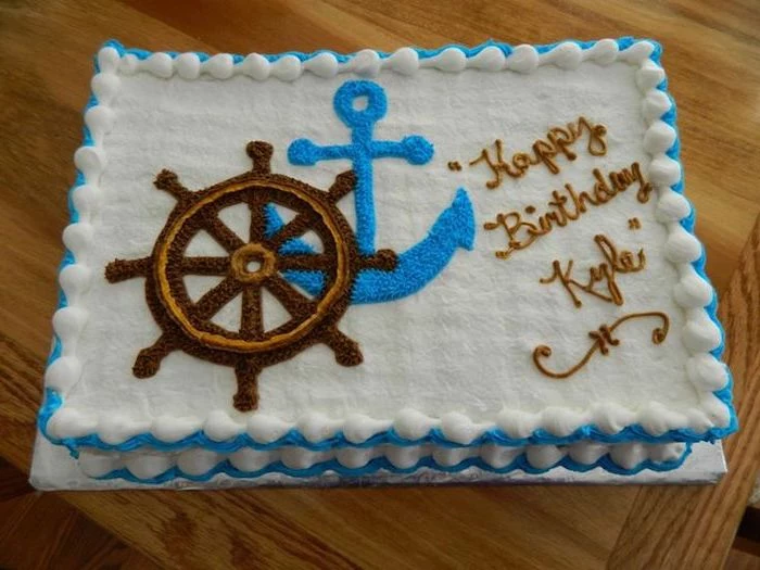 steering wheel of a ship, in brown and beige, and a blue anchor, painted in frosting, on a white rectangular cake, nautical baby shower cakes 