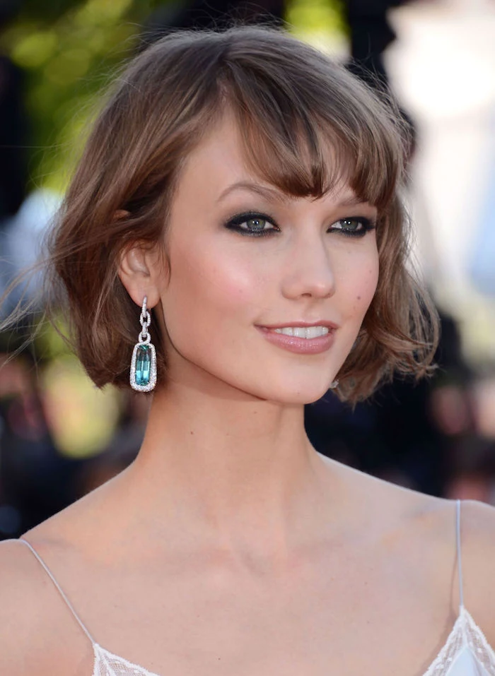karlie kloss with a short, wavy brunette bob, wearing a white strappy top, dark eye make up, and a glossy pale pink lipstick, short haircuts for thin hair 