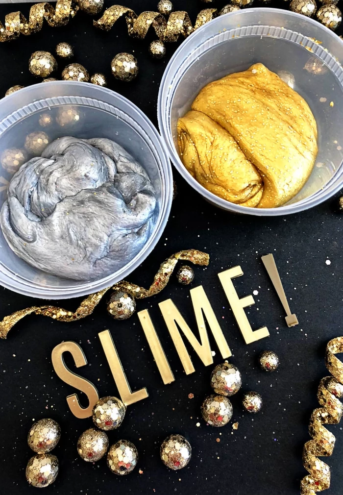 how to make slime with borax, two plastic pots, containing silver and gold metallic slime, placed on a black surface, near some glittering golden decorations