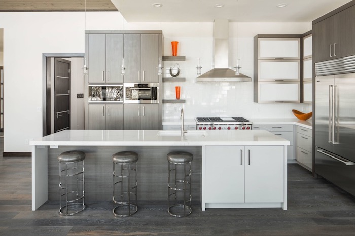 stools in metallic grey, near a white counter top, inside a kitchen with grey, and metallic silver cabinets, with splashes of orange, white subway tile 