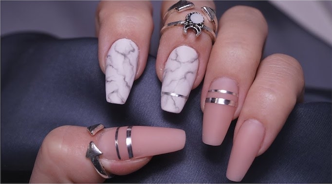 stripes made from a silver metallic substance, decorating the coffin nails of a hand, gripping a dark grey fabric, two of the nails are white, with marble pattern, white the other three are matte nude pink