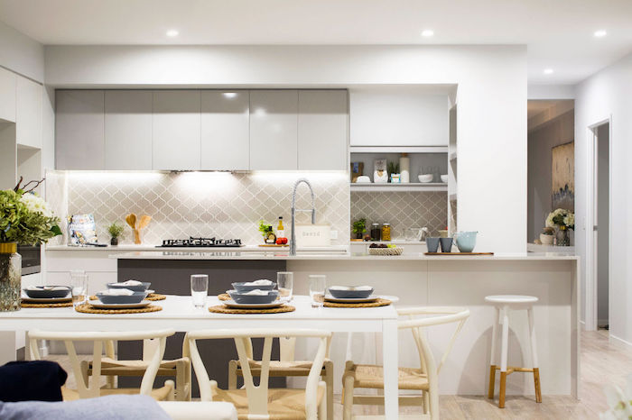 dining table in white, with several chairs, near a kitchen area, with pale grey cabinets, and an arabesque backsplash, in a similar hue