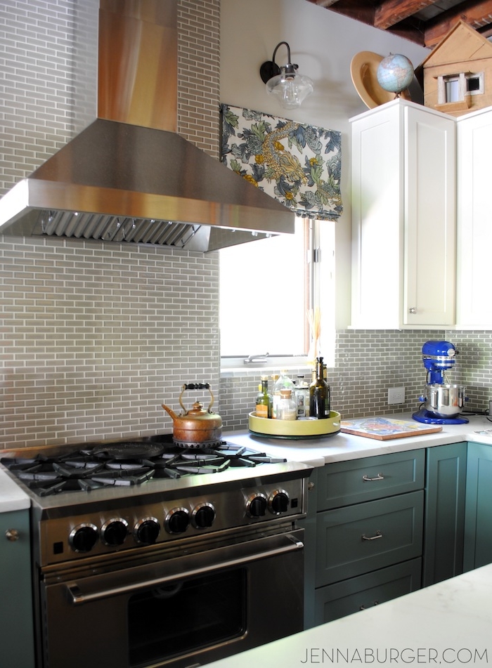 teal and white cabinets and drawers, in a kitchen with a metal oven, and a matching extractor hood, small grey subway tile pattern on the wall 