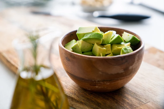 chopped avocado in small wooden bowl, placed on wooden board, basil pesto recipe