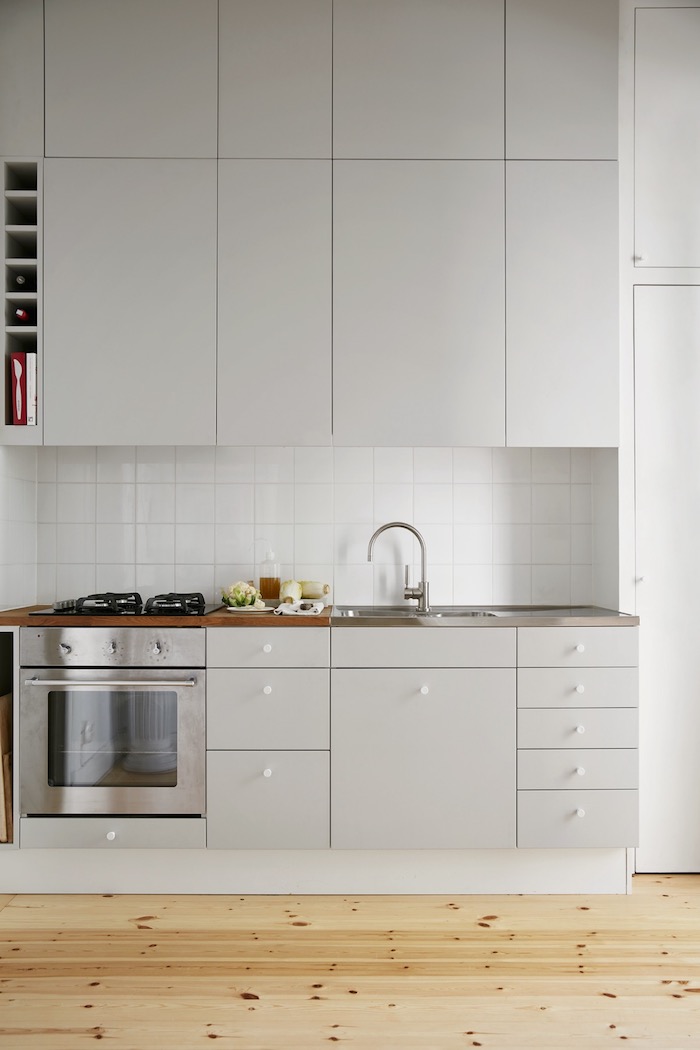 square tiles on a white kitchen backsplash, in a room with white cabinets, shiny metal oven, and a beige wooden floor