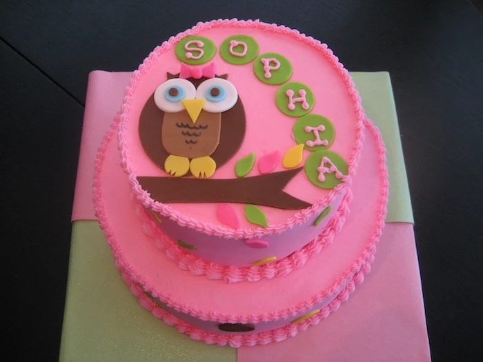 bubblegum pink two-layered cake, decorated with brown owl figurine, made from fondant, and green buttons, with pale pink frosting, spelling out the name sophia, owl baby shower cake