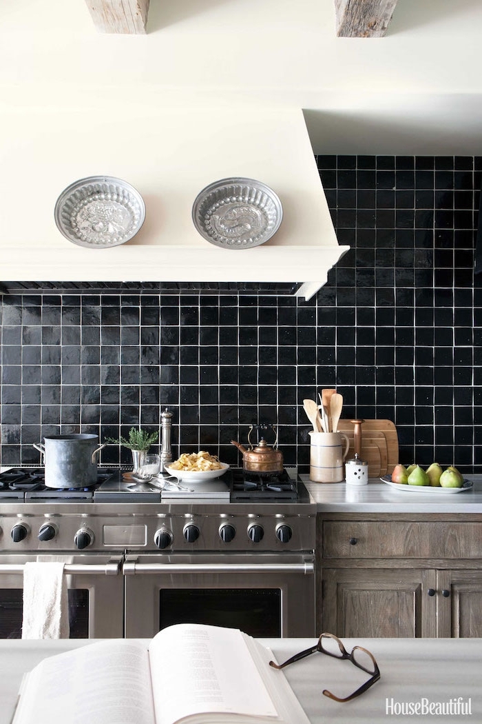 vintage style kitchen, with a wall covered in smooth, square black tiles, grayish-brown cabinets, two ovens with stoves