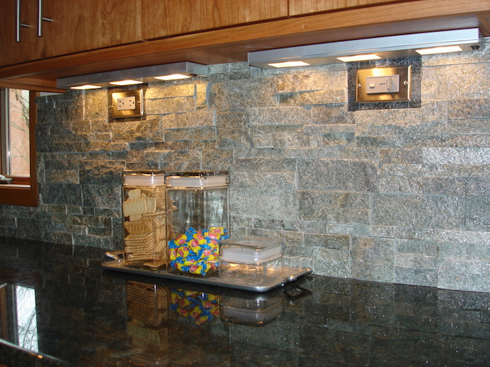 biscuits and candy, in two glass containers, on a black counter top, grey stacked stone backsplash, wooden kitchen cabinets