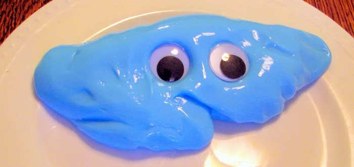 round white plate, containing a smooth, shiny bright blue pile of slime, decorated with two large googly eyes, in black and white