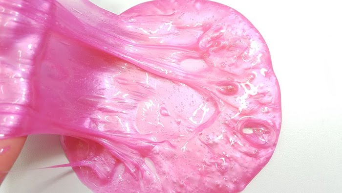 stretching a piece of bubblegum pink, silky and sticky elmer's glue slime, partially stuck to a white smooth surface