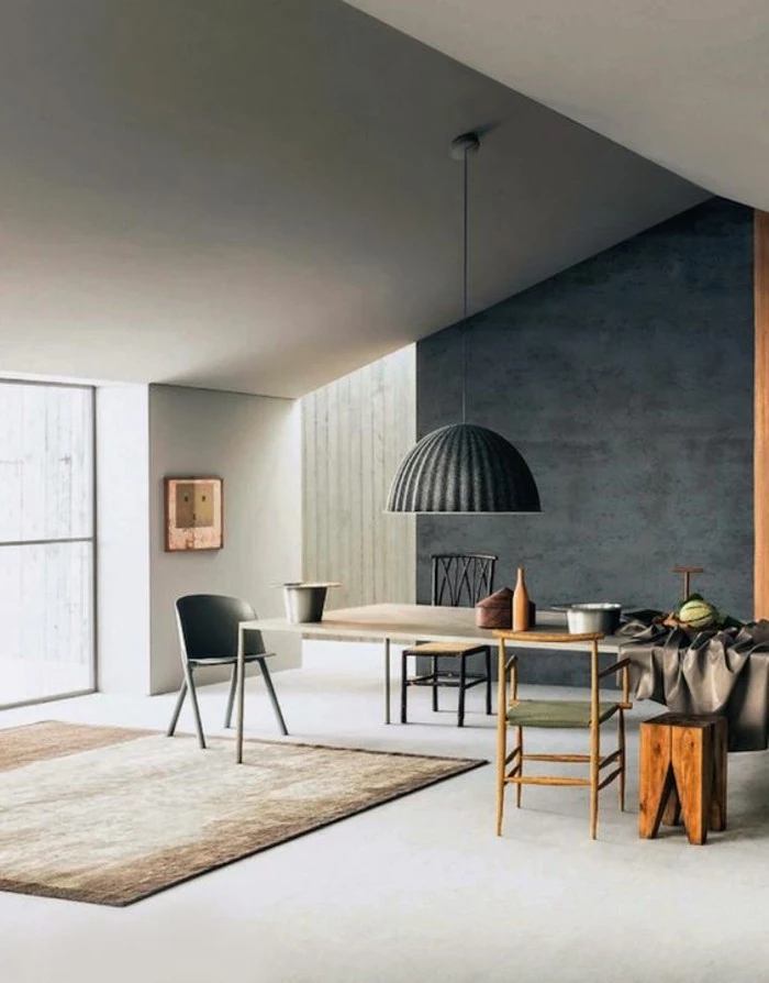 dining table with three mismatched chairs and a stool, inside a room with a sloped ceiling, white floor and light grey walls, a dark grey accent wall