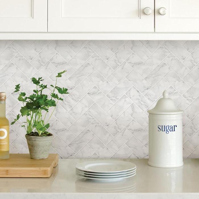 parsley planted in a small grey pot, and placed on a wooden cutting board, three white plates, and a sugar container, on a pale grey counter, herringbone backsplash in light grey