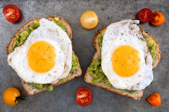 cherry tomatoes in halves, easy breakfast recipes, two pieces of bread, smeared with guacamole, and topped with black pepper dusted fried egg