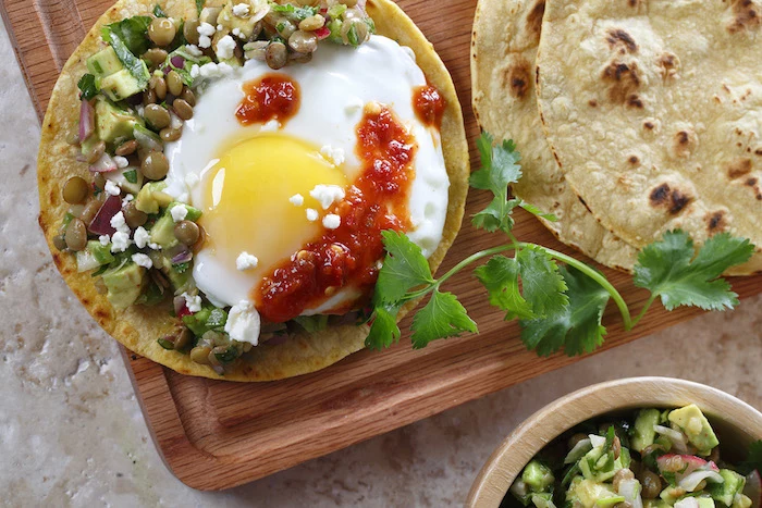 lentils and avocado, veggies and salsa, and a sunny side up runny egg, on a breakfast taco, more tacos and chutney, and a sprig of cilantro